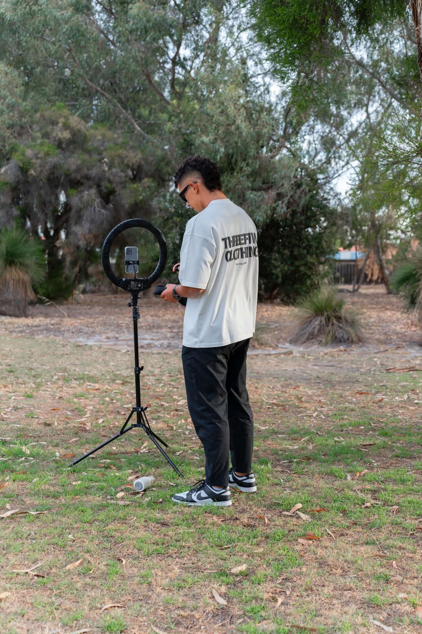 Male wearing white Tshirt, standing in a park