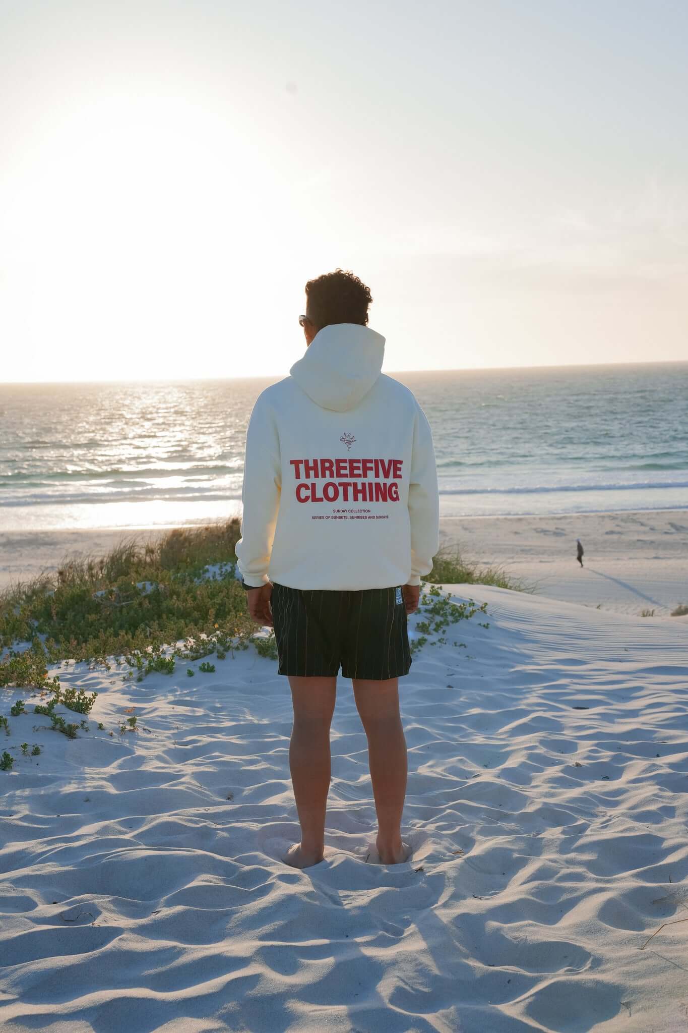 Male wearing vanilla coloured hoodie, standing, admiring the sunset at a beach