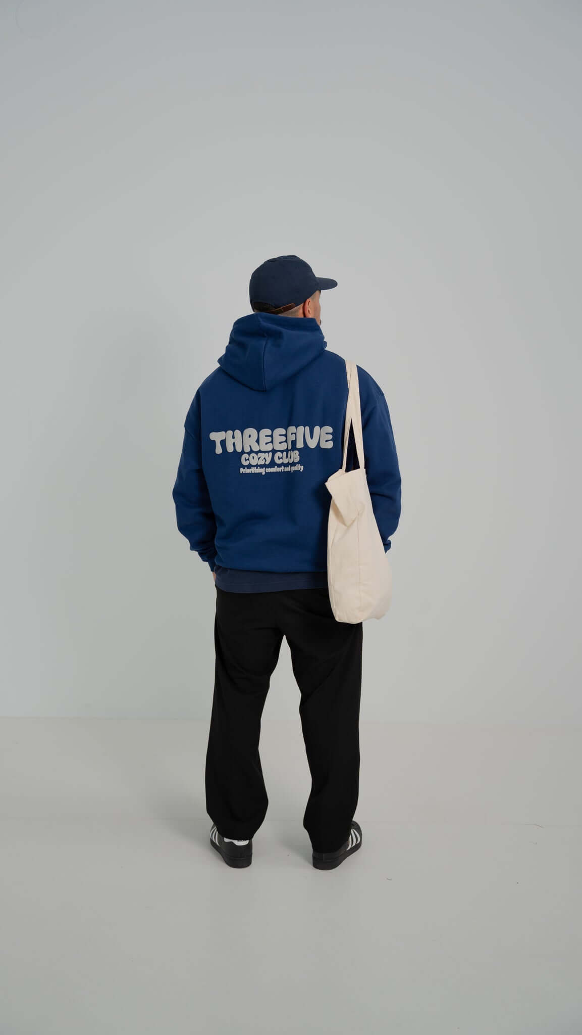 Male standing confidently wearing deep sea blue v2 hoodie, tote bag over shoulder