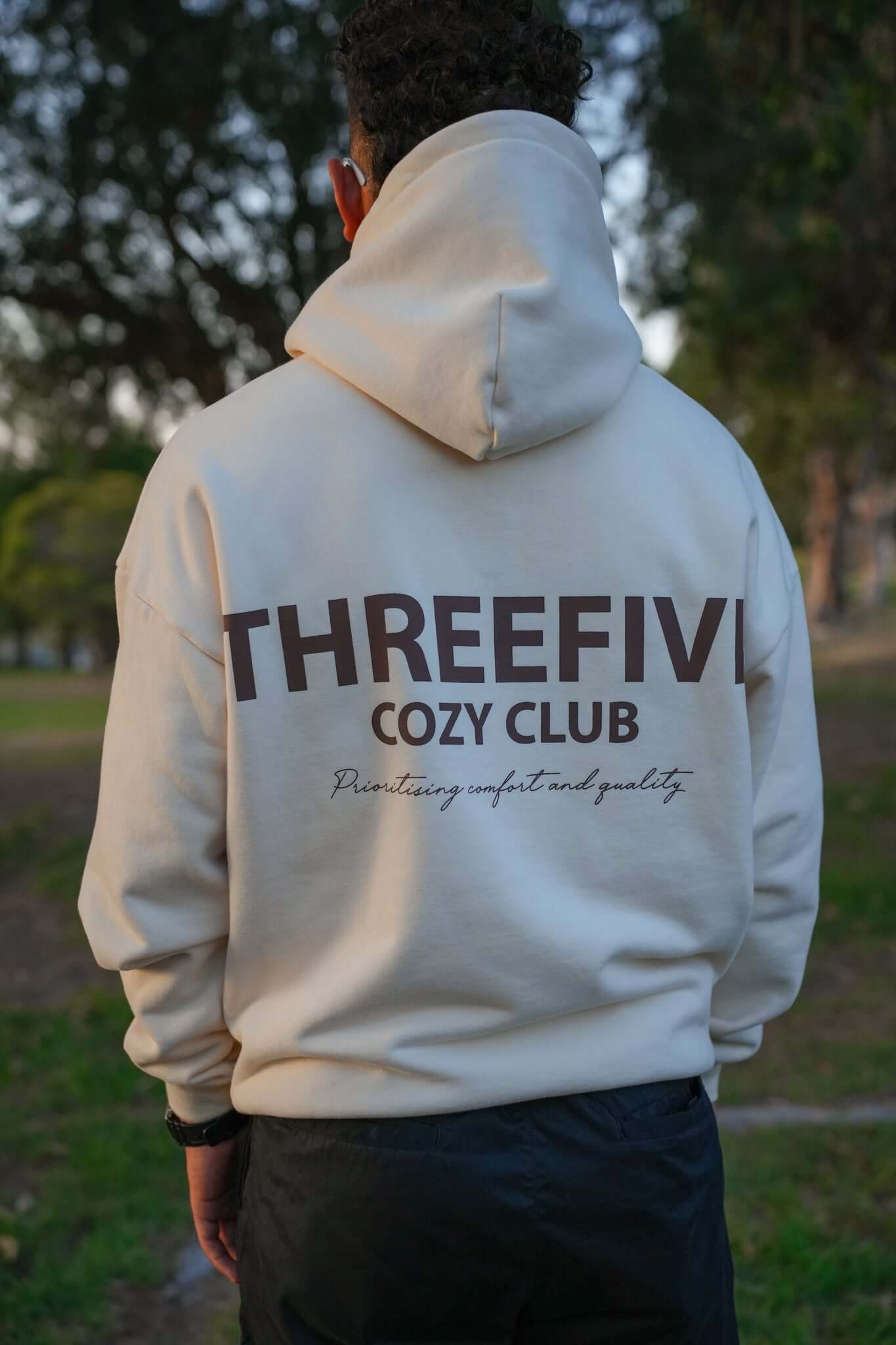 Male wearing a cream cozy club hoodie from ThreeFive Clothing, pictured from the back