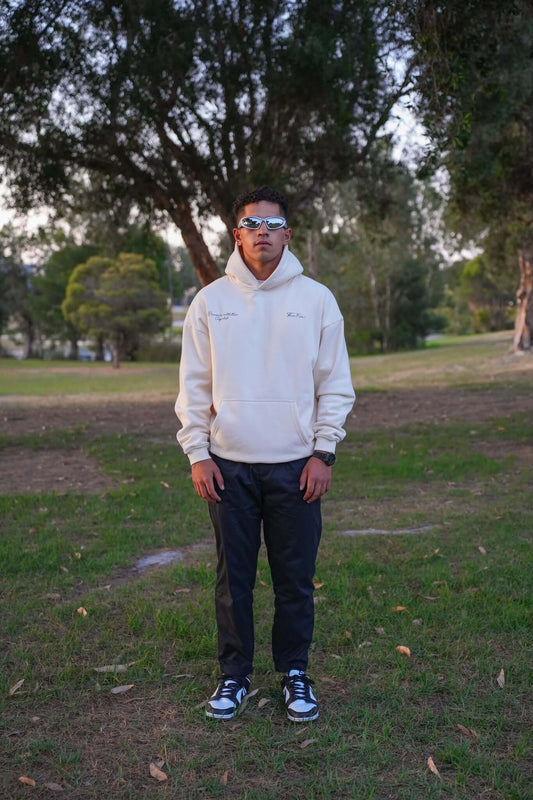 Male wearing sunglasses and a oversized cream hoodie from ThreeFive Clothing, standing confidently amidst the serene beauty of a park.
