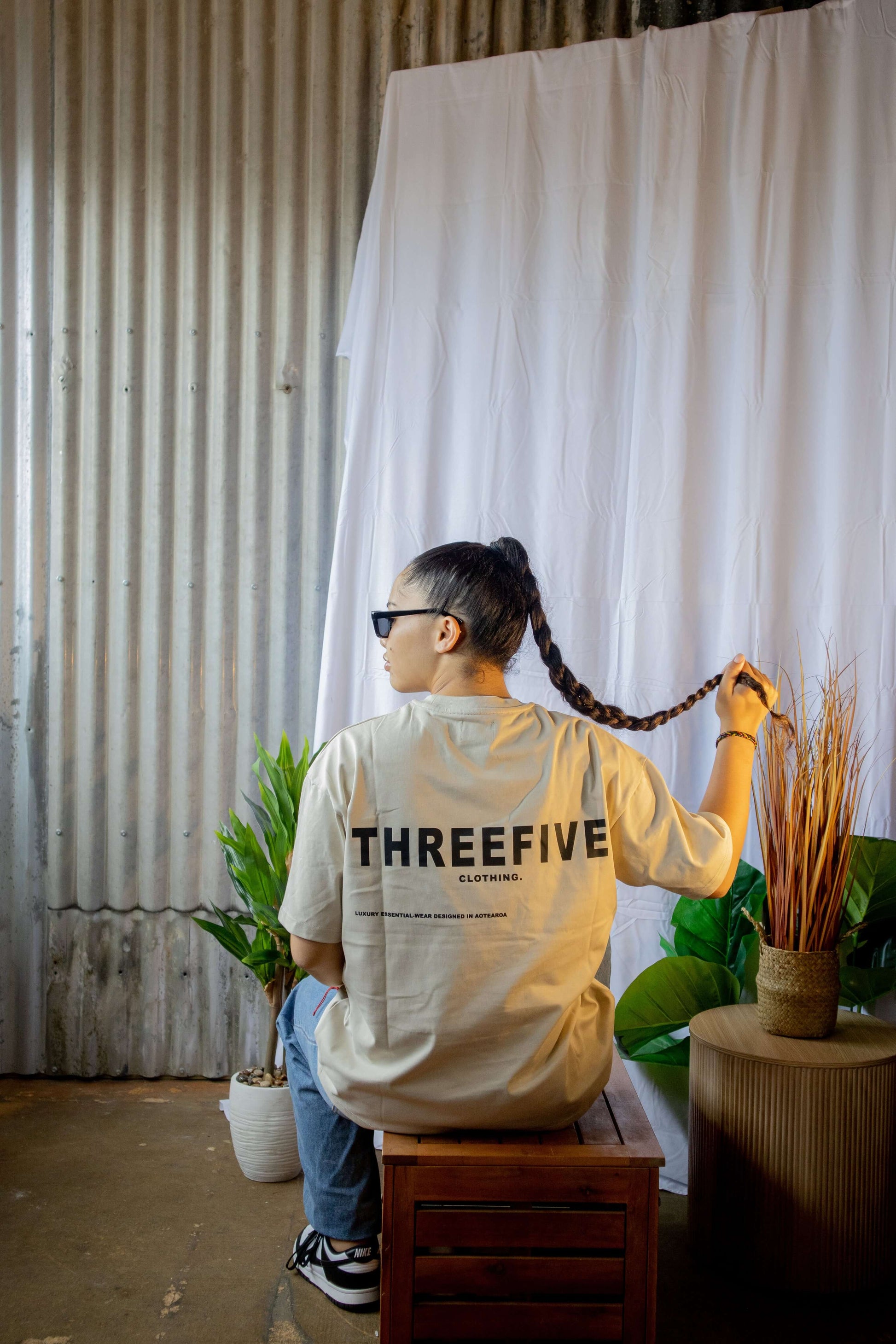 Female sitting, wearing bone coloured ThreeFive T-shirt, pictured from the back